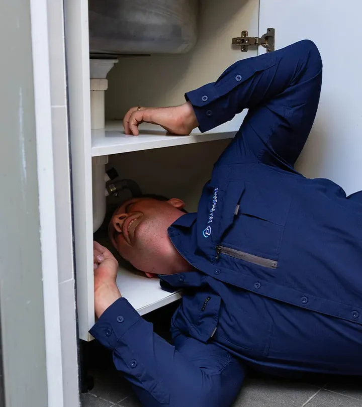 Plumber lying on the floor to reach the pipework inside a cupboard under a sink