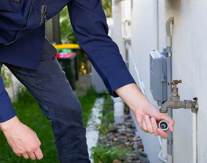 Plumber fitting a hose connector to a brass garden tap on an outside wall