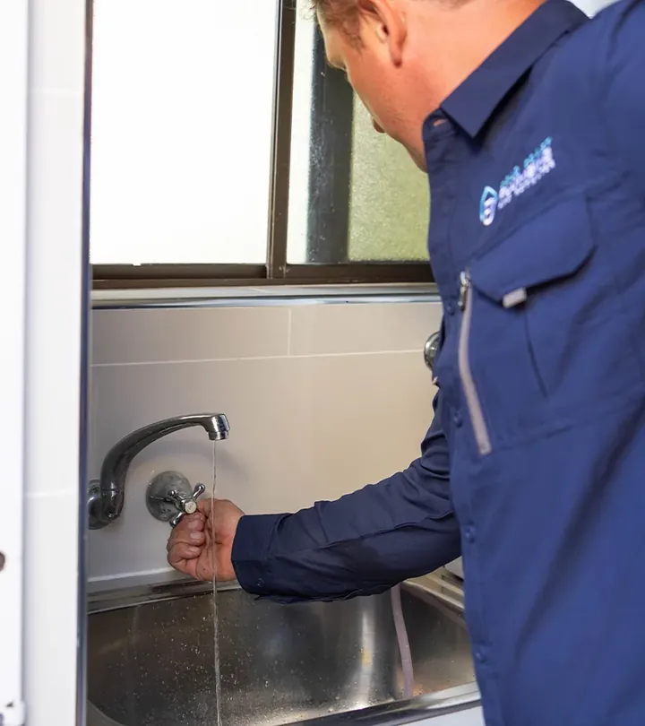 Plumber turning on a laundry tap with water running into a stainless steel sink