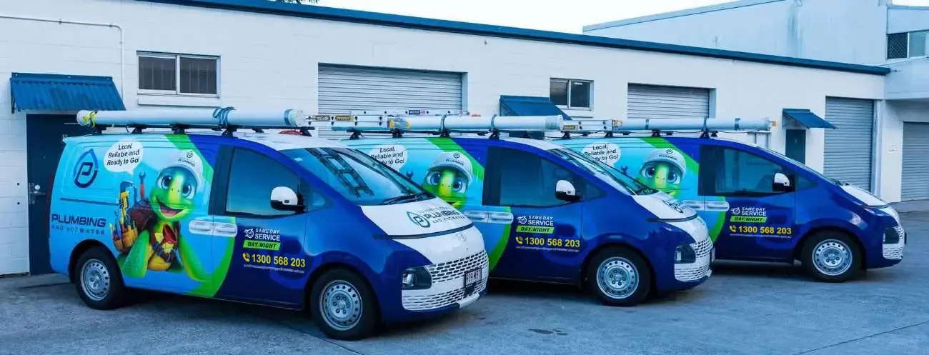 Three blue and green sign-written plumbing vans with roof racks parked outside a workshop