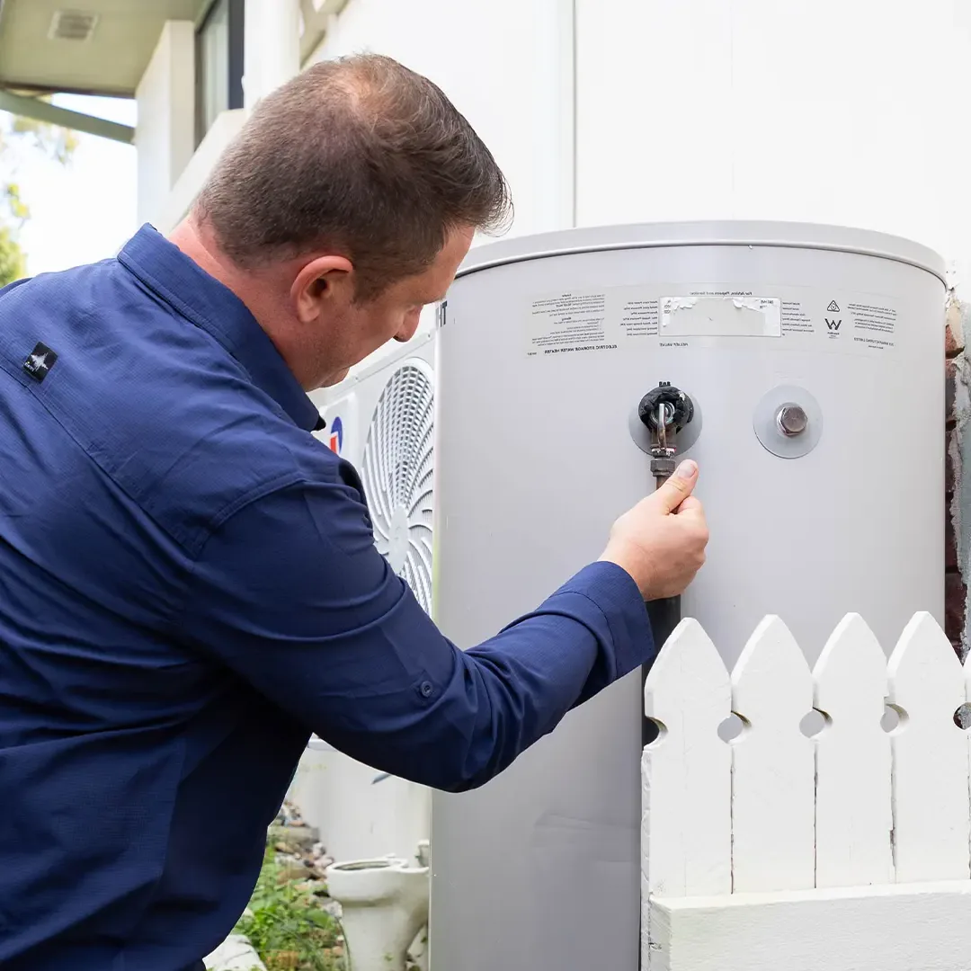 Plumber commissioning a new electric storage hot water tank with a heat pump unit installed beside it